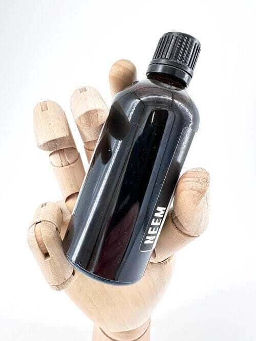 Wooden hand holding neem oil bottle against a white background for natural product advertisement.